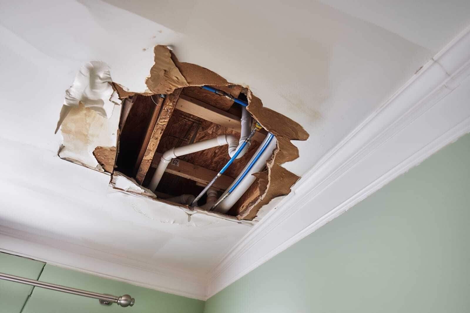 Water damage restoration technician extracting water from hallway after burst pipe — professional equipment and visible wall damage